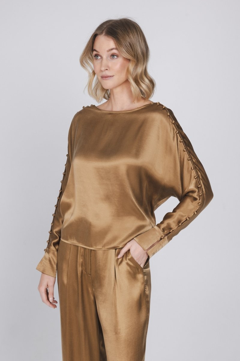 Een model met blond, golvend haar poseert tegen een lichtgrijze achtergrond | Accentil Moda Blouse Mokka | Jo&Co Club