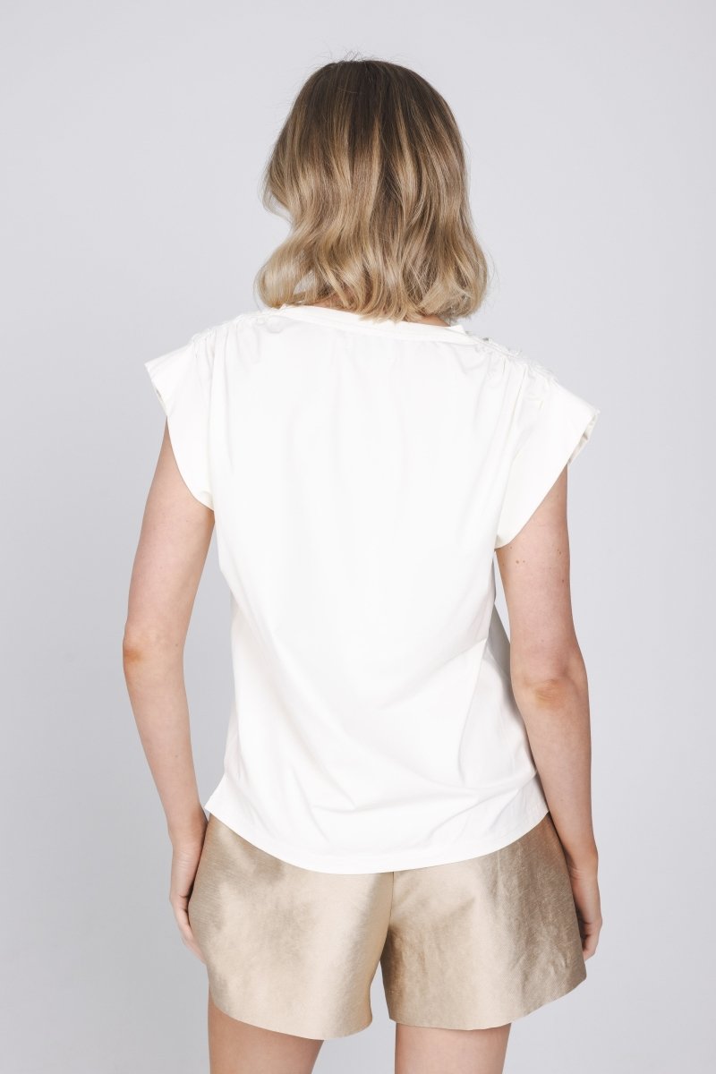 Een model, van achteren gefotografeerd, draagt een gebroken witte top met kapmouwen | Accentil Nivi Top White | Jo&Co Club