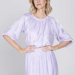 Een model met blond, halflang golvend haar staat gefotografeerd tegen een effen | Accentil Sere Blouse Lila | Jo&Co Club