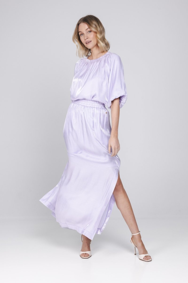Een model met blond, golvend haar poseert in een lila-kleurige outfit tegen een | Accentil Vela Skirt Lila | Jo&Co Club