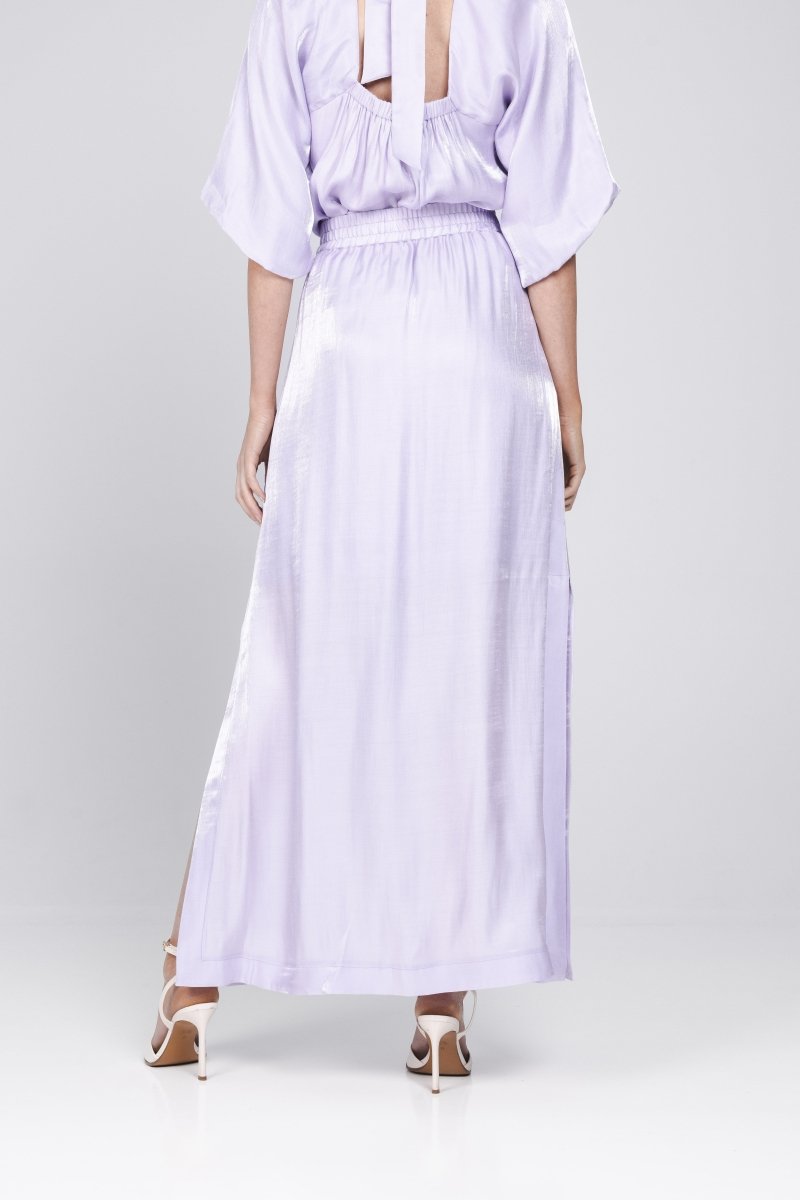 Een model, van de achterkant gefotografeerd, draagt een lange, lila rok met een | Accentil Vela Skirt Lila | Jo&Co Club
