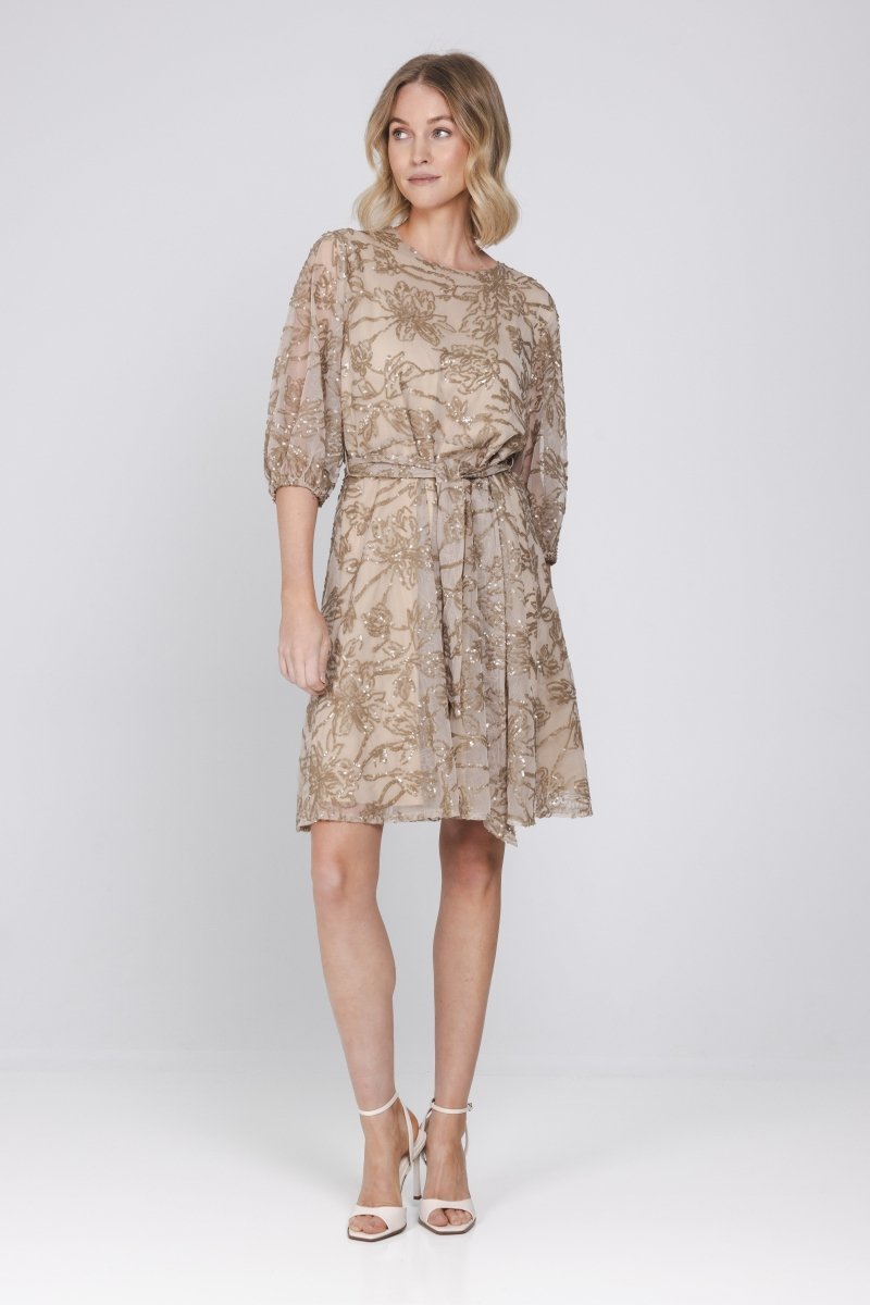 Een model staat frontaal op een lichte, egale achtergrond en draagt een zandkleurige | Accentil Vive Dress Sand | Jo&Co Club