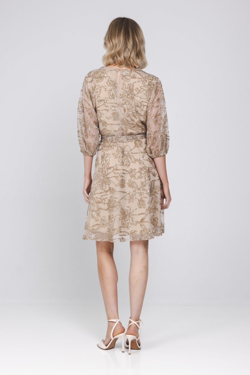 Een model, van achteren gefotografeerd, draagt een knielange, zandkleurige jurk | Accentil Vive Dress Sand | Jo&Co Club