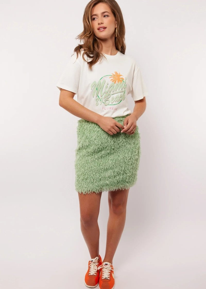 Model draagt de mintgroene Arianne Skirt van Fluresk met een wit T-shirt en oranje sneakers, perfect voor een zomerse casual look.