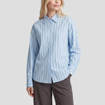 Gestreepte blouse Fluresk Joan in lichtblauw – oversized, op een grijze wijde pantalon | Jo&Co Club