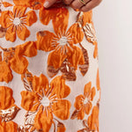 Detailopname van de oranje bloemenprint op de Mindy Skirt van Fluresk, met glanzende afwerking en zichtbare textuur.