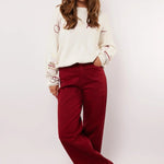 Model draagt de Fluresk Verina Pants in bordeauxrood met witte trui en zwarte laarzen.