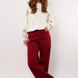 Model draagt de Fluresk Verina Pants in bordeauxrood met witte trui en zwarte laarzen.