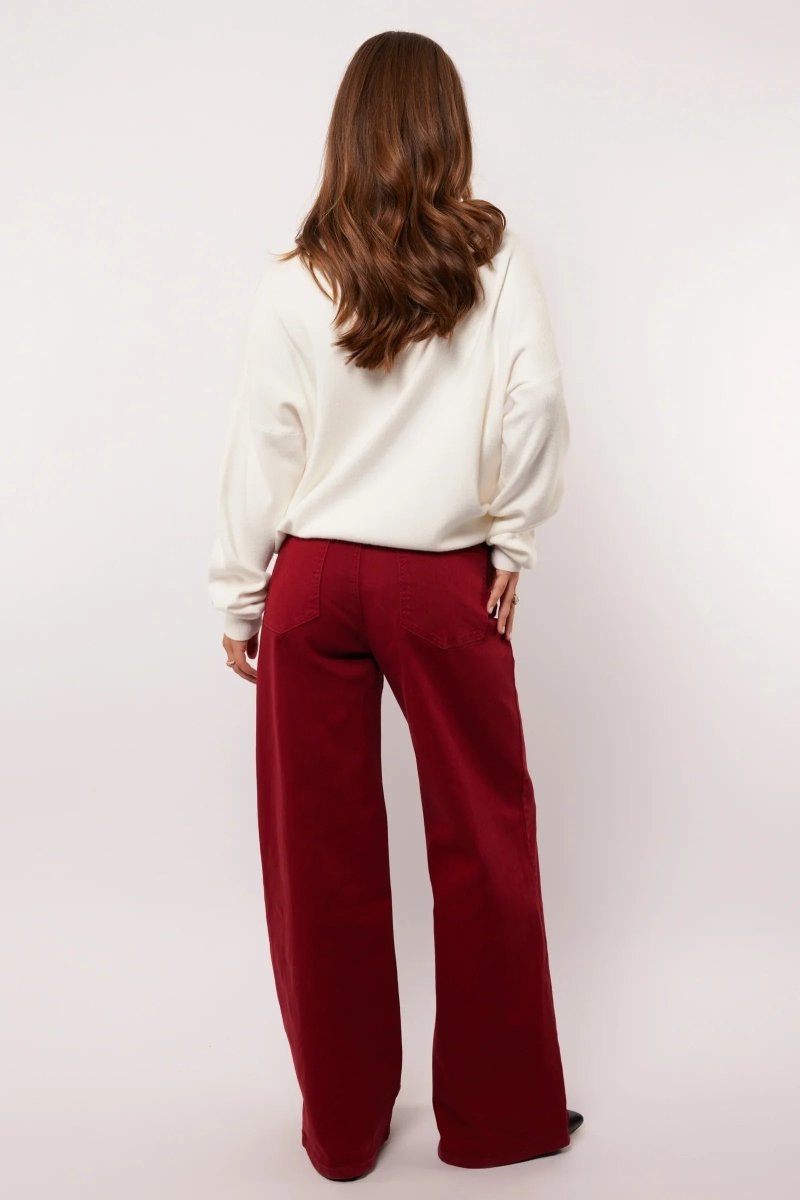 Vrouw draagt bordeauxrode wide leg broek van Fluresk, gezien van achteren.
