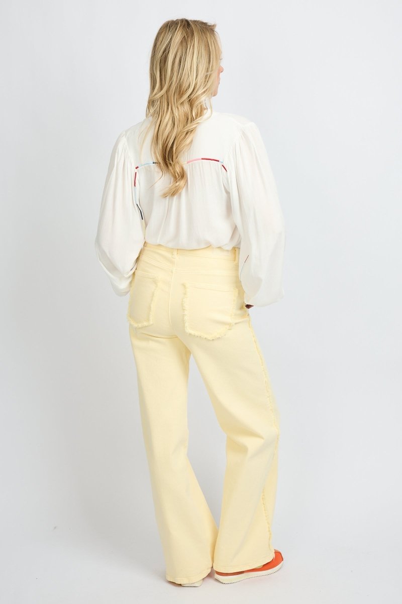 Model draagt de Verina Pants van fluresk in het butter yellow met een hoge taille voor dames samen met de Yailin blouse met pofmouwen in het off-white.