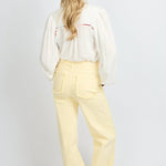 Model draagt de Verina Pants van fluresk in het butter yellow met een hoge taille voor dames samen met de Yailin blouse met pofmouwen in het off-white.