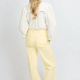 Model draagt de Verina Pants van fluresk in het butter yellow met een hoge taille voor dames samen met de Yailin blouse met pofmouwen in het off-white.