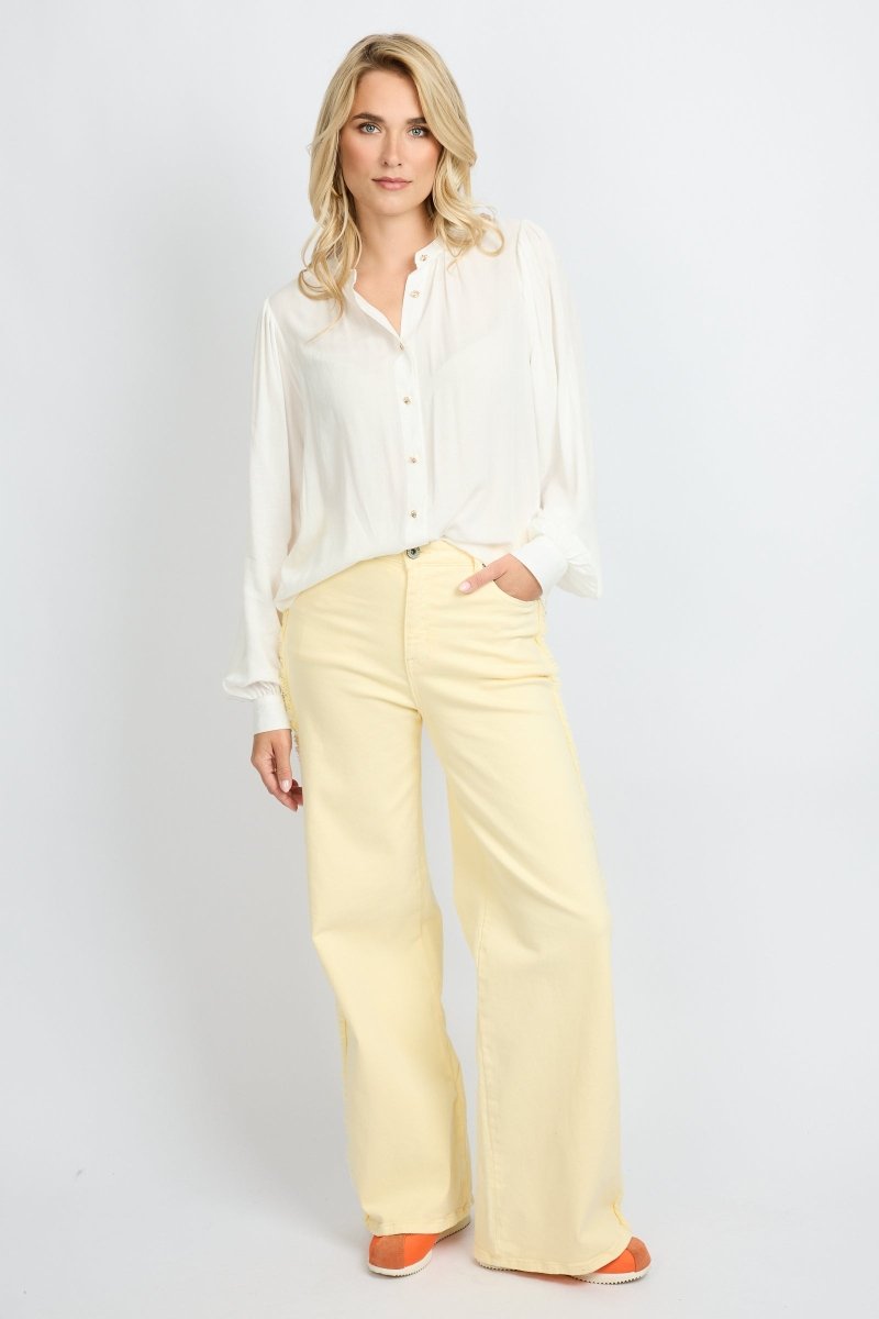 Model draagt de Verina Pants van fluresk in het butter yellow met een hoge taille voor dames samen met de Yailin blouse met pofmouwen in het off-white.