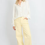 Model draagt de Verina Pants van fluresk in het butter yellow met een hoge taille voor dames samen met de Yailin blouse met pofmouwen in het off-white.