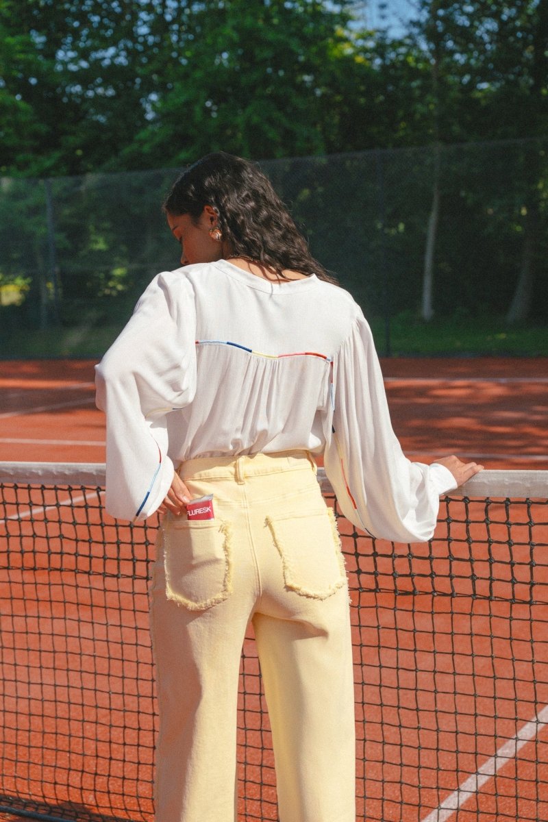 Model draagt de Verina Pants van fluresk in het butter yellow met een hoge taille voor dames samen met de Yailin blouse met pofmouwen in het off-white.