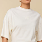 Model in crème boxy t-shirt met logo HEYB Club, andere kant | Jo&Co Club