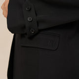 Detail zwarte blazer Jadie – mouwlipje met drie knoopjes en klepzak met logo | Jo&Co Club