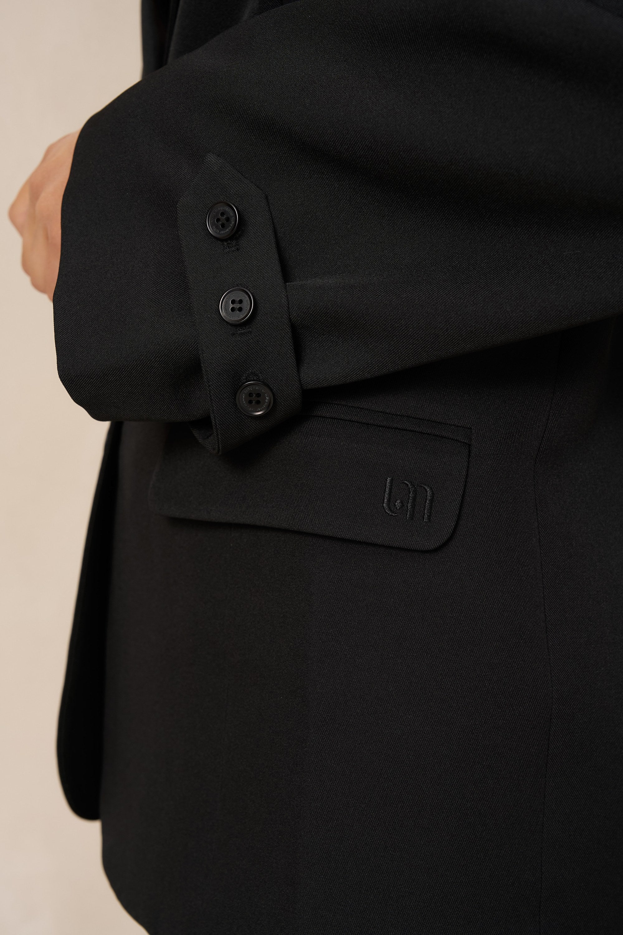 Detail zwarte blazer Jadie – mouwlipje met drie knoopjes en klepzak met logo | Jo&Co Club