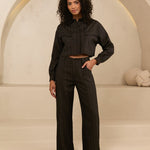 model draagt de viola blouse en de janna pants van lofty manner. het is een zwart pak met gouden krijtstreep.