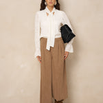 Model in crème blouse Jett met strik, gedragen op een bruine ribcord broek | Jo&Co Club