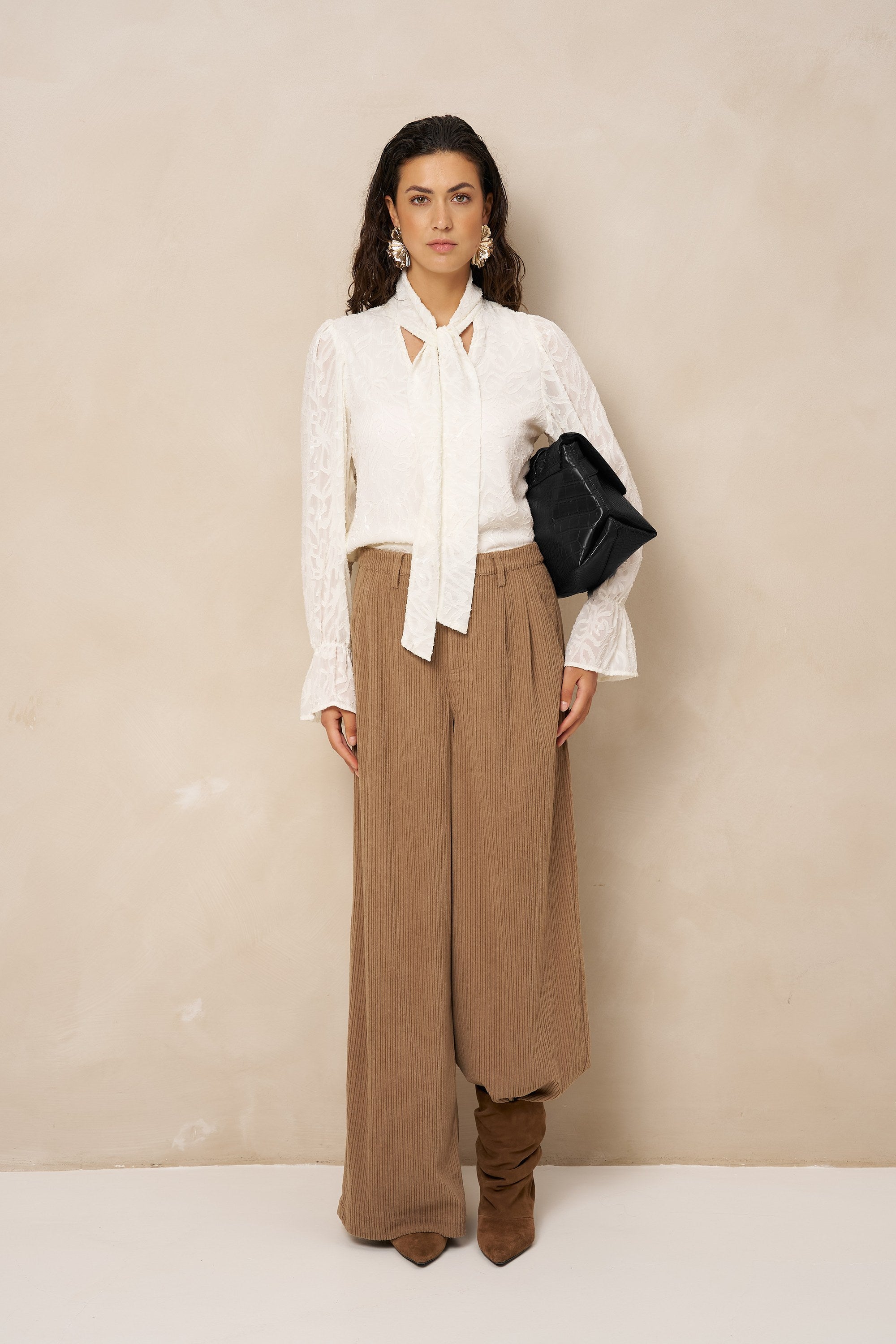 Model in crème blouse Jett met strik, gedragen op een bruine ribcord broek | Jo&Co Club