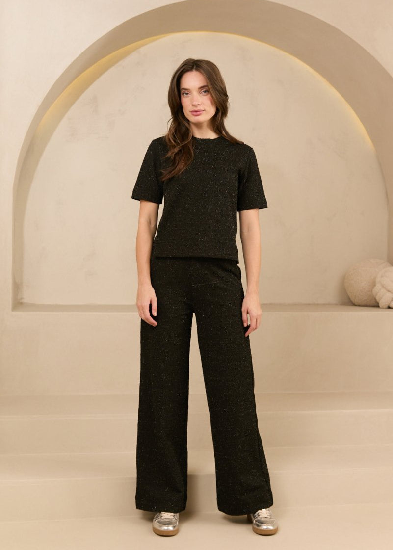 model draagt de dora trouser en de eva top van lofty amnner, het is een co-ord set in het zwart met glinstering.