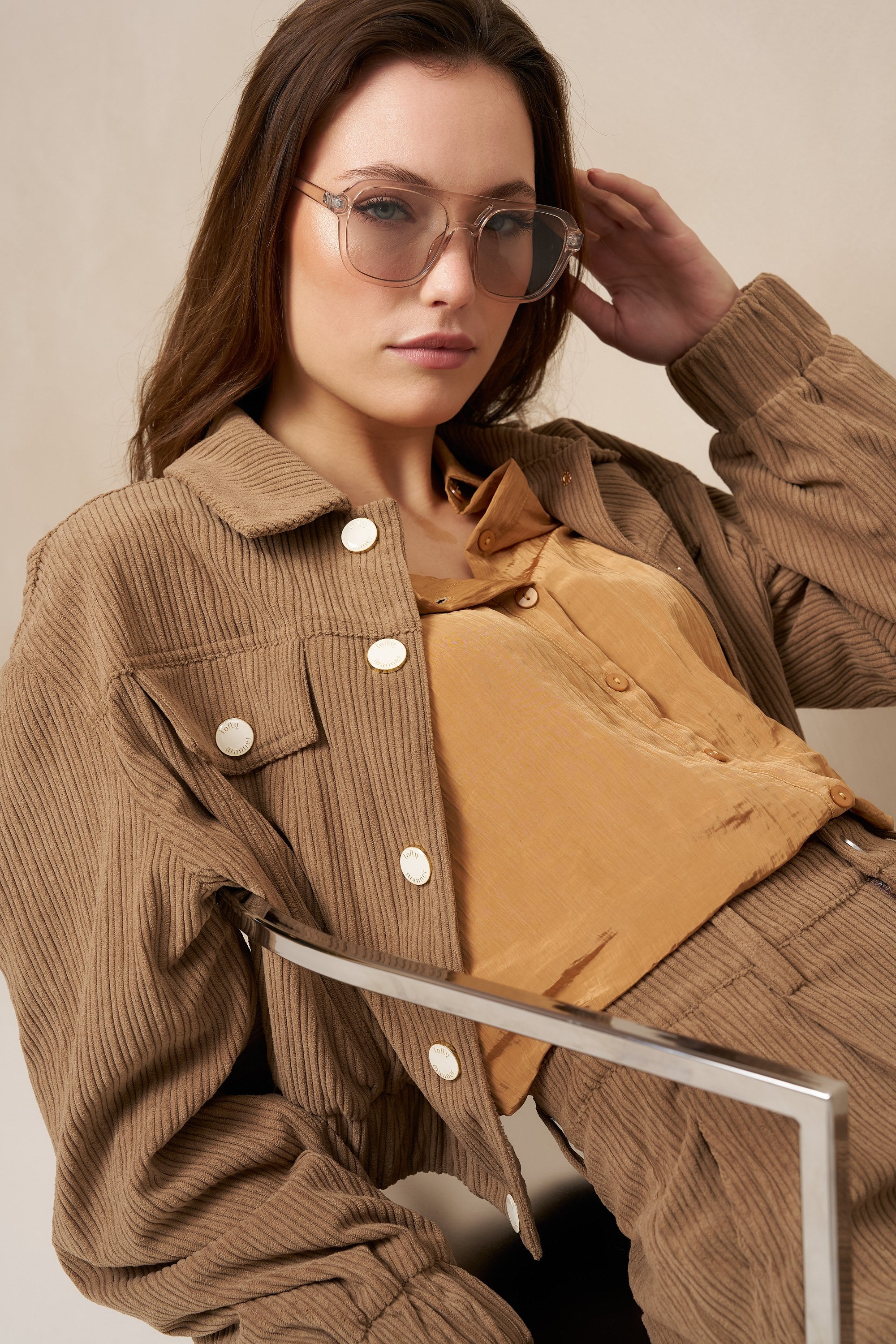 Model zittend in taupe ribcord jasje Jaxy met okergele blouse en zonnebril | Jo&Co Club