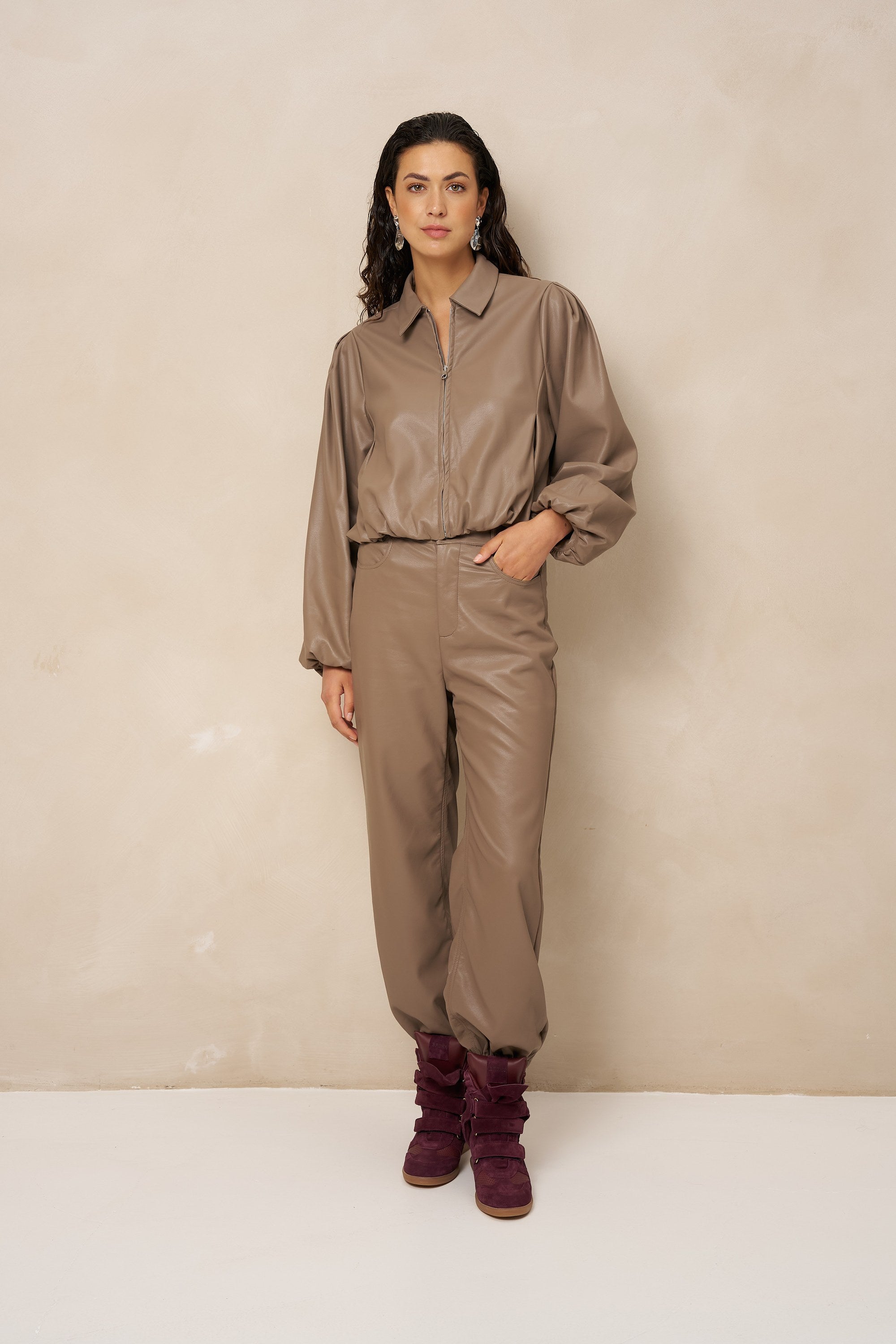 Model in taupe kunstleren jack Jillie met bijpassende broek en bordeaux laarzen | Jo&Co Club