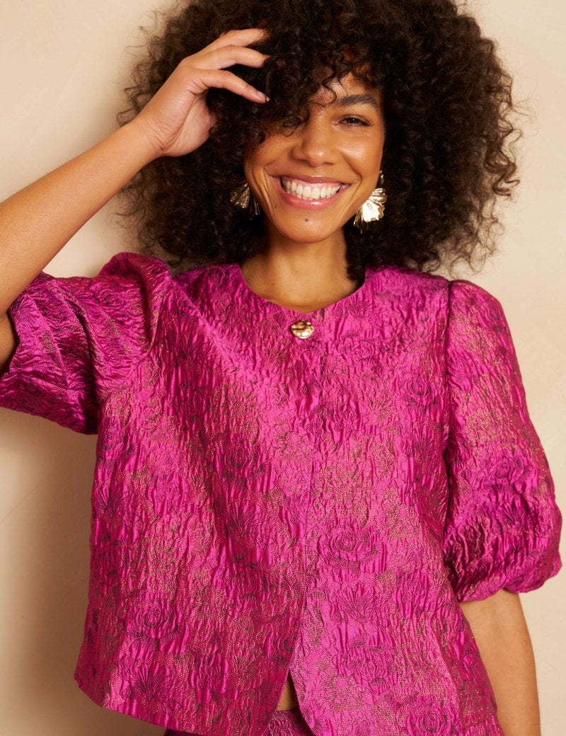 Close-up van een lachend model met volumineus krullend haar dat een fuchsia jacquard top | Lofty Manner Gianna | Jo&Co Club
