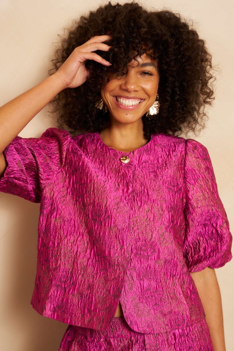 Close-up van een lachend model met volumineus krullend haar dat een fuchsia jacquard top | Lofty Manner Gianna | Jo&Co Club