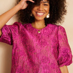 Close-up van een lachend model met volumineus krullend haar dat een fuchsia jacquard top | Lofty Manner Gianna | Jo&Co Club