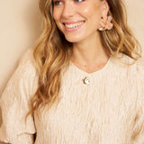 Een model met lang, golvend blond haar draagt een crèmekleurige top met een opvallende | Lofty Manner Gianna | Jo&Co Club