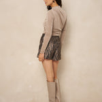 Model van opzij in taupe gedrapeerde top Jimmi en hoge taupe laarzen | Jo&Co Club
