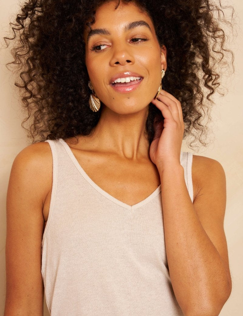Een model met bruin krullend haar staat tegen een effen, beige achtergrond | Lofty Manner Nicki | Jo&Co Club