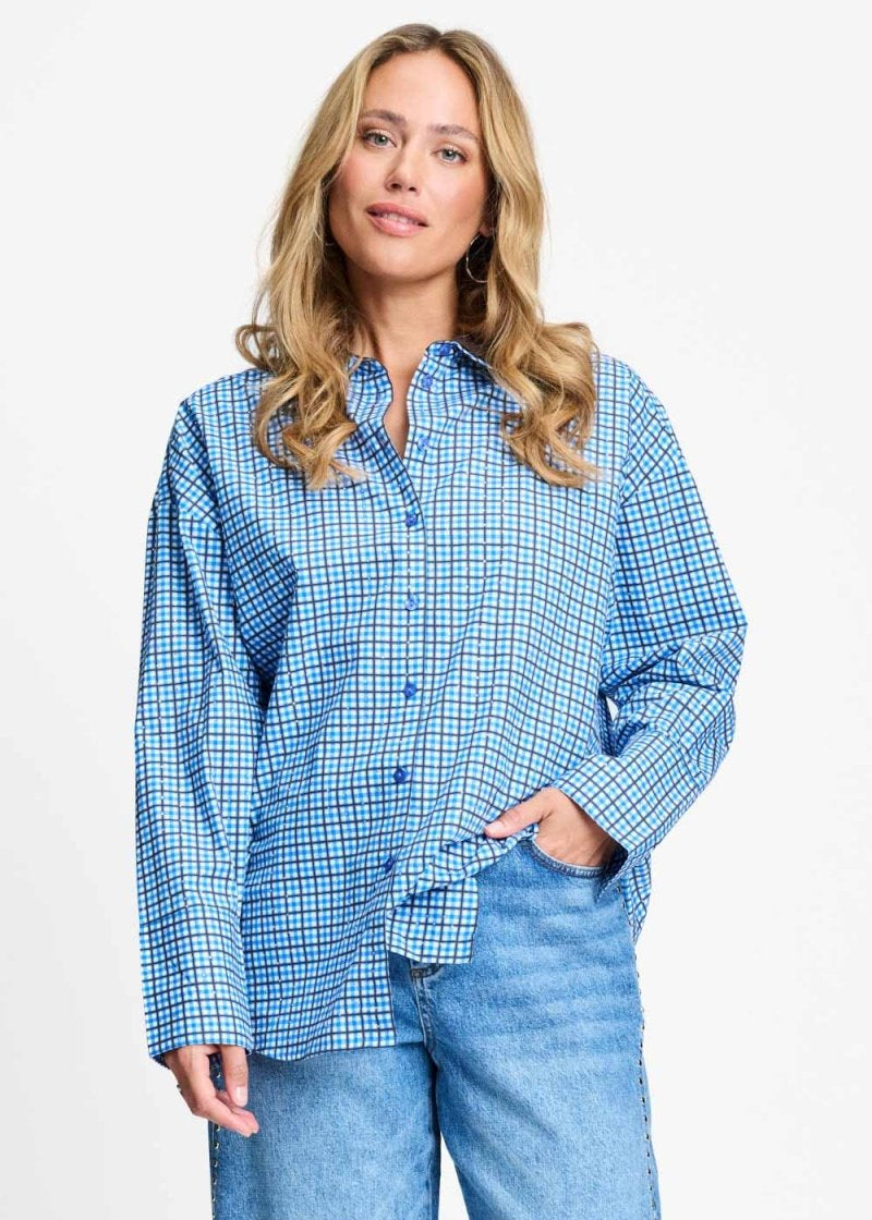 Model draagt de saffierblauwe geruite Beau Check blouse van POM Amsterdam op een lichtblauwe jeans.