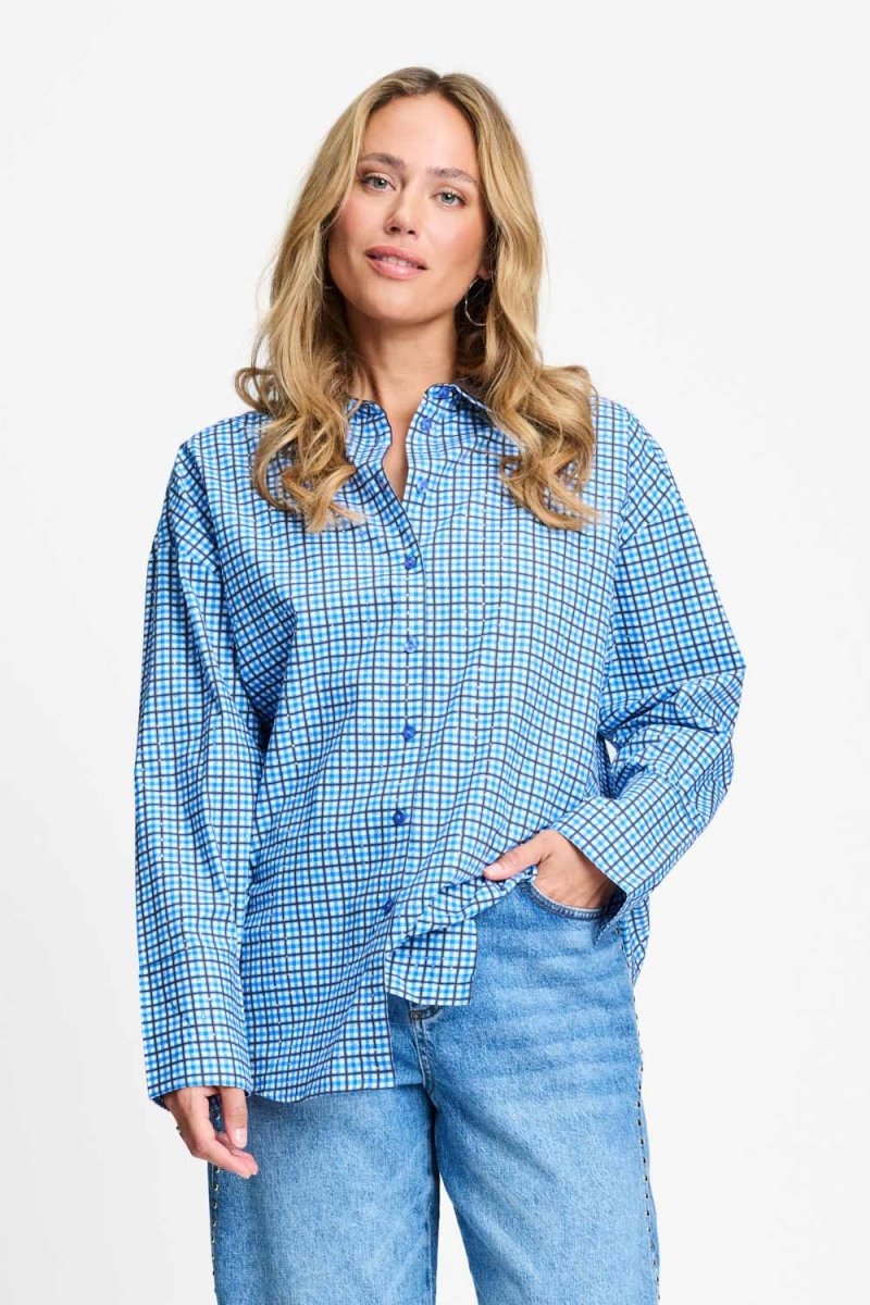 Model draagt de saffierblauwe geruite Beau Check blouse van POM Amsterdam op een lichtblauwe jeans.