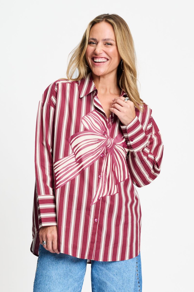 Model draagt de donkerrood gestreepte Beau Ribbon blouse van POM Amsterdam met grote strikprint.