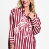 Model draagt de donkerrood gestreepte Beau Ribbon blouse van POM Amsterdam met grote strikprint.