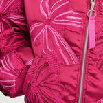 Detailfoto van het strikborduursel en de rits met roze lintje op de bomberjas.