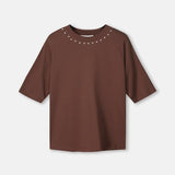 Productfoto van het bruine t-shirt plat gefotografeerd, met studs rond de hals.