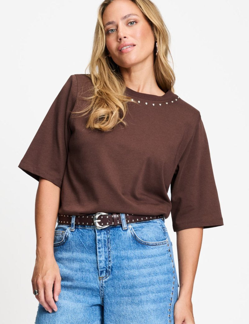 Model draagt het chocoladebruine t-shirt Taylor van POM Amsterdam op een lichte jeans.