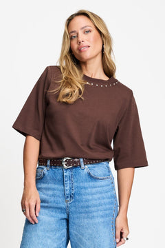 Model draagt het chocoladebruine t-shirt Taylor van POM Amsterdam op een lichte jeans.
