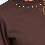 Detailfoto van de zilverkleurige studs rond de halslijn van het bruine t-shirt.