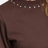 Detailfoto van de zilverkleurige studs rond de halslijn van het bruine t-shirt.