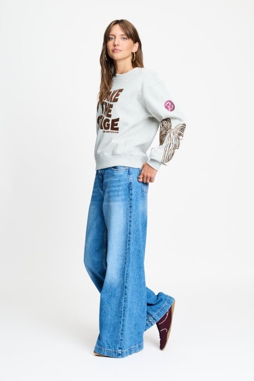 Volledige look met de grijze sweater op een wijde lichtblauwe jeans.