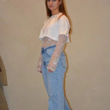 Model draagt een lichtblauwe jeans met een rechte pasvorm en subtiele wassing, gestyled met een witte cropped top en kanten details voor een trendy look.