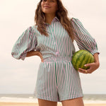 Model draagt de Annie blouse en Belle short van Ydence als co-ord set op het strand – zomerse look met streepjesprint.