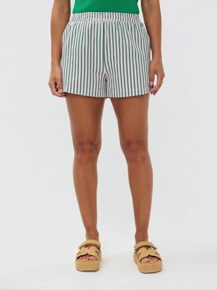 Model draagt de Belle short,een luchtige wit-lila gestreepte short met elastische tailleband van Ydence, ideaal voor het strand.