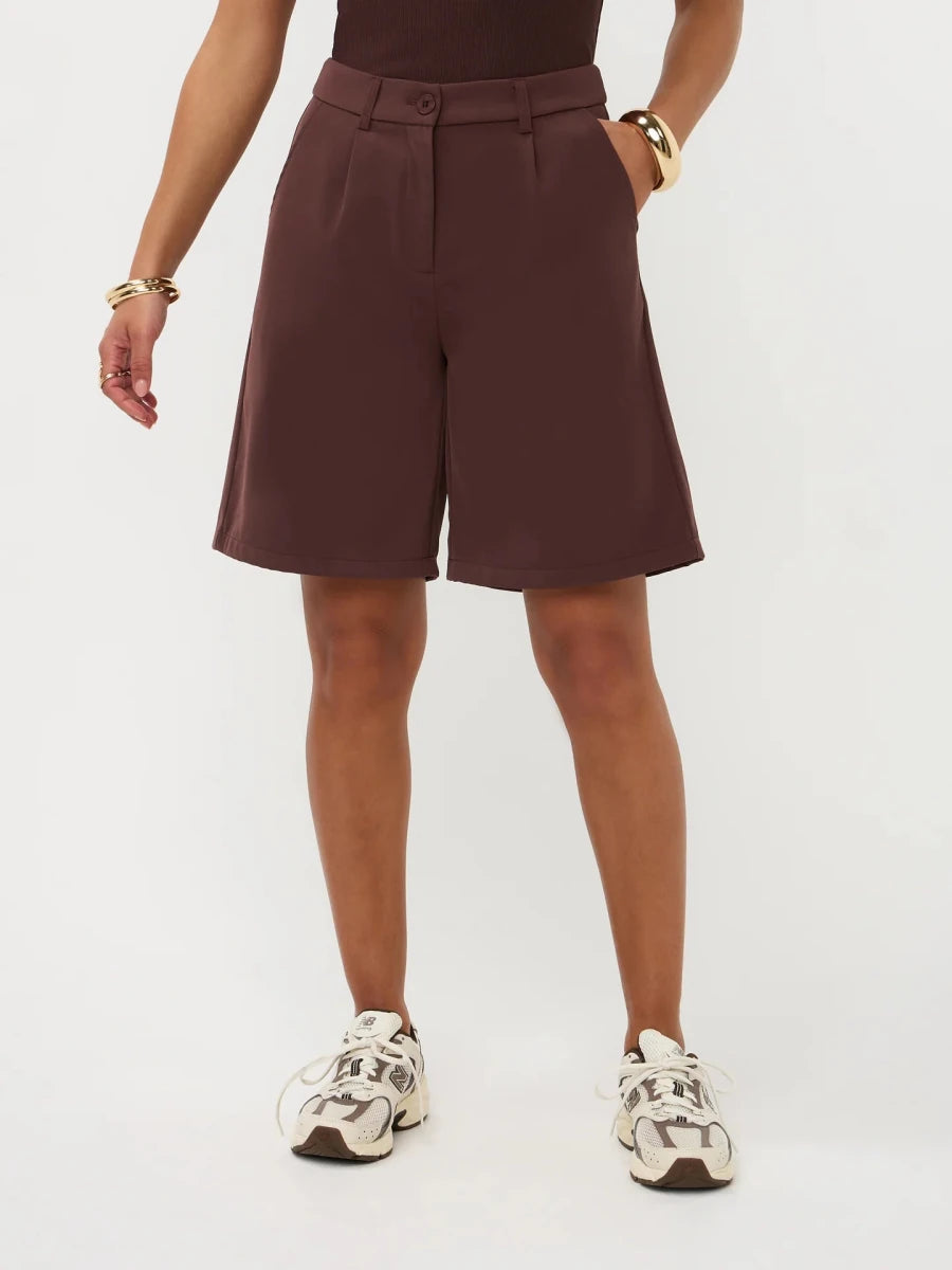 Een model, zichtbaar vanaf de taille, draagt een wijdvallende, donkerbruine bermuda short | Ydence Jolijn | Jo&Co Club
