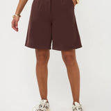 Een model, zichtbaar vanaf de taille, draagt een wijdvallende, donkerbruine bermuda short | Ydence Jolijn | Jo&Co Club